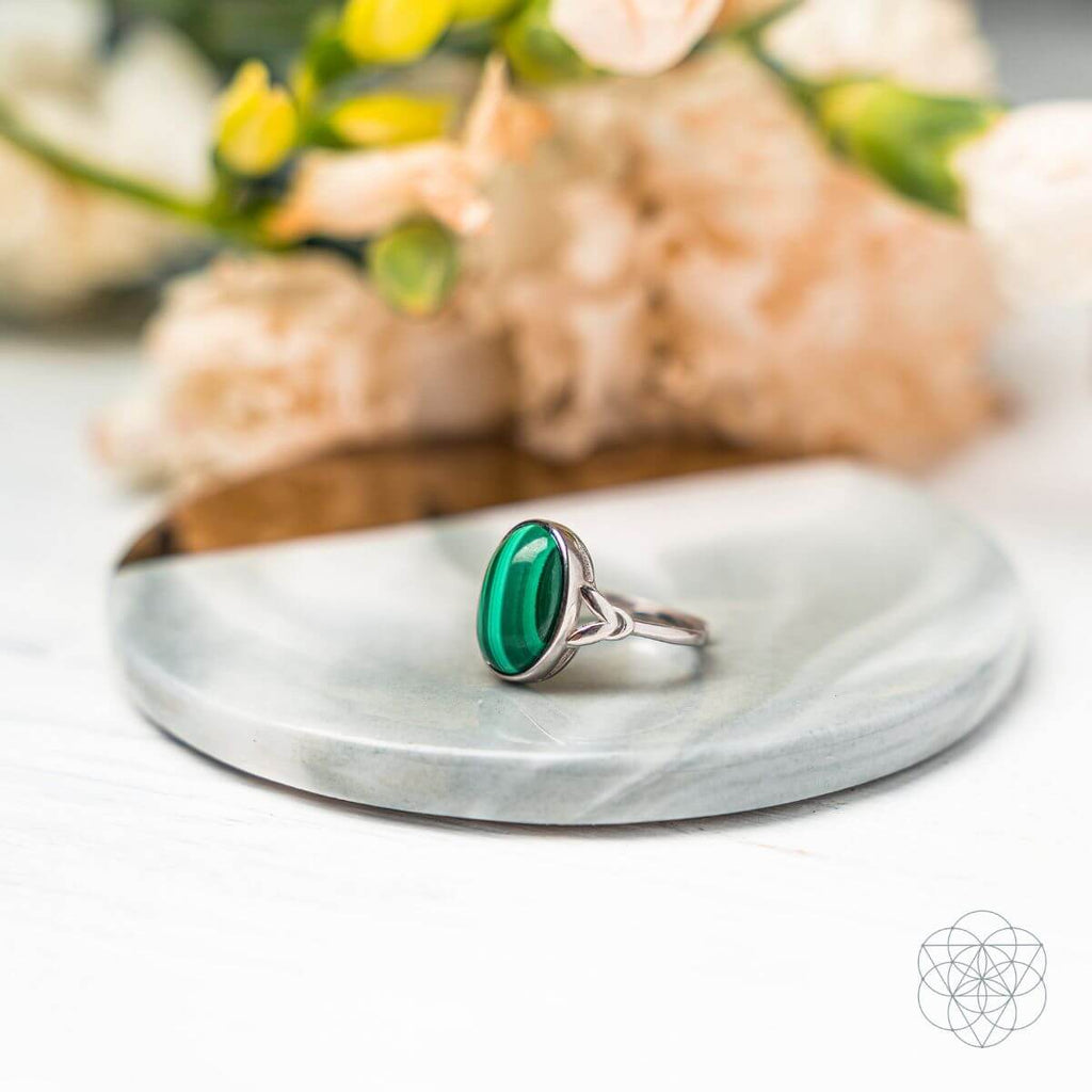 Silver ring with a green stone on a marble surface with flowers in the background