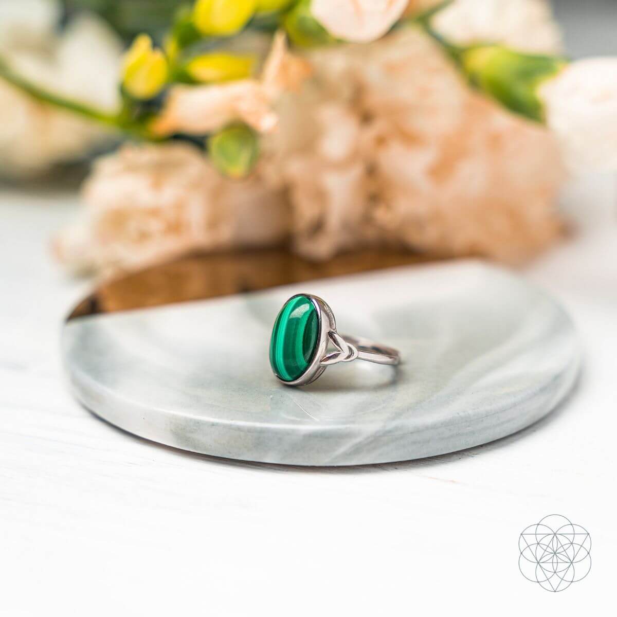 Silver ring with a green stone on a marble surface with flowers in the background
