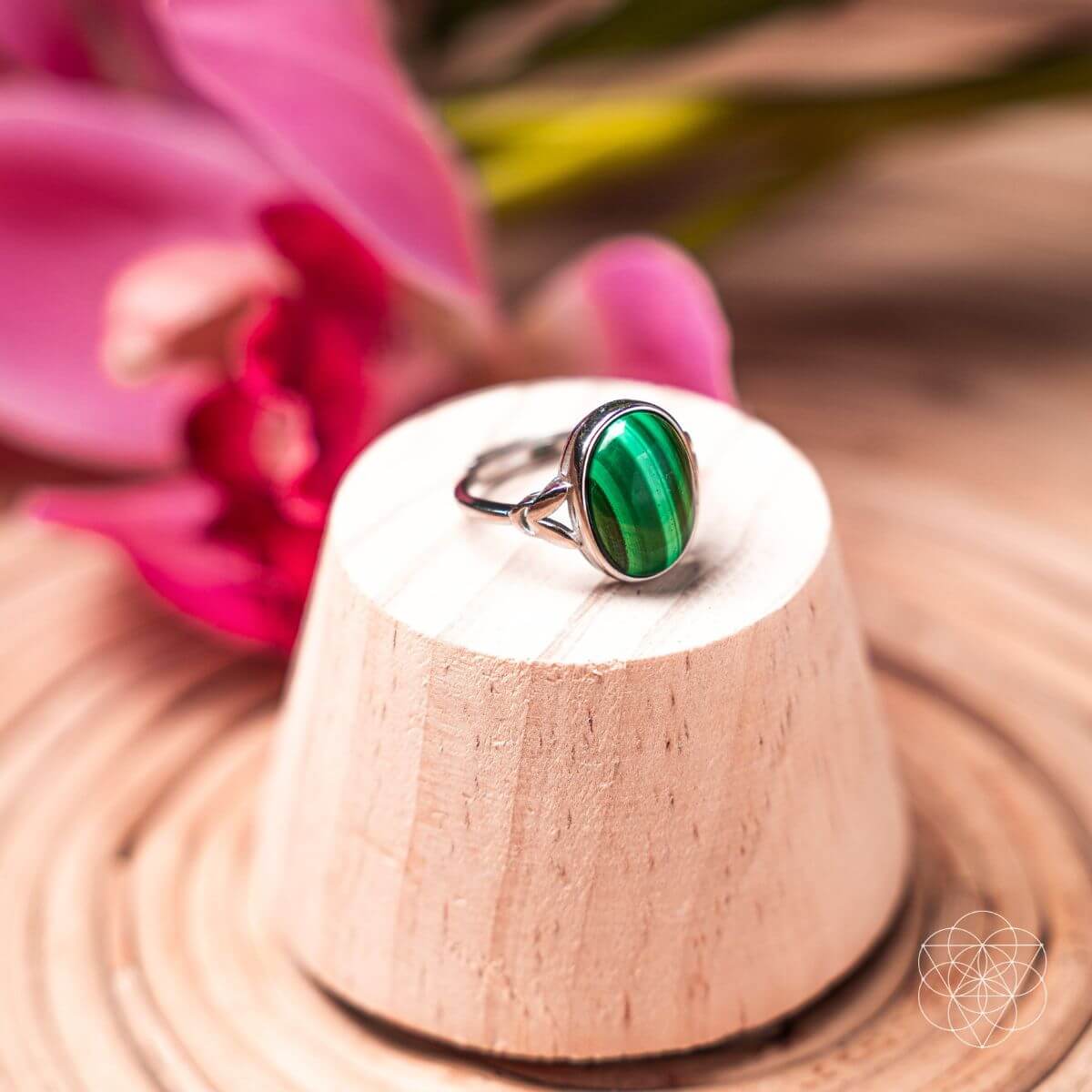 Green ring on a wooden stand with a pink flower in the background