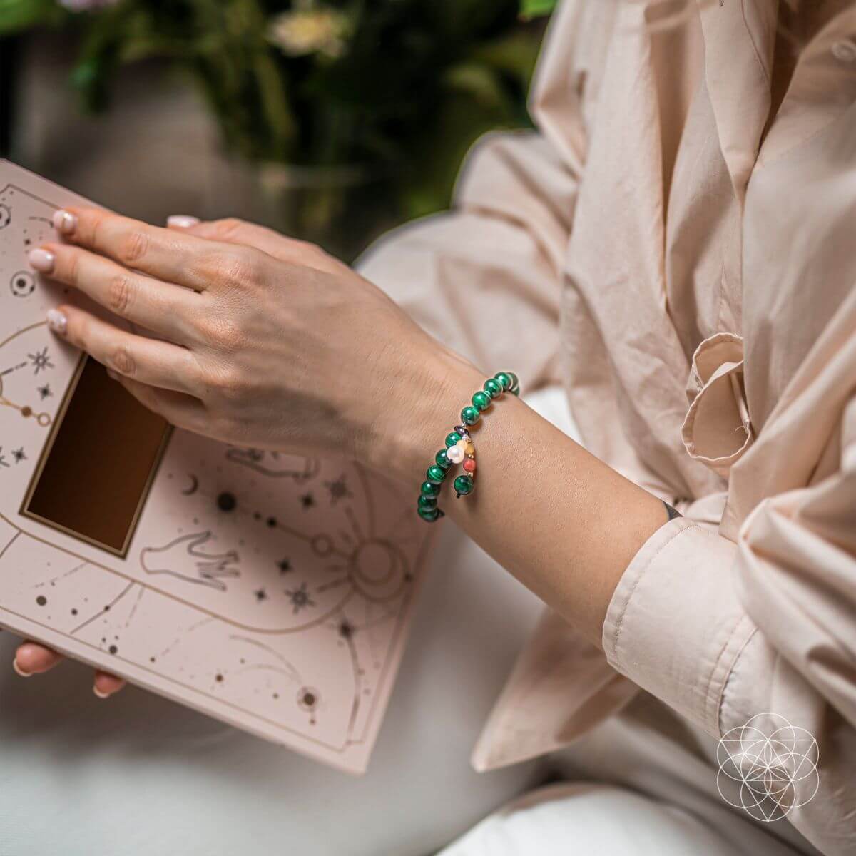 Person holding a tarot card deck with a green beaded bracelet on wrist