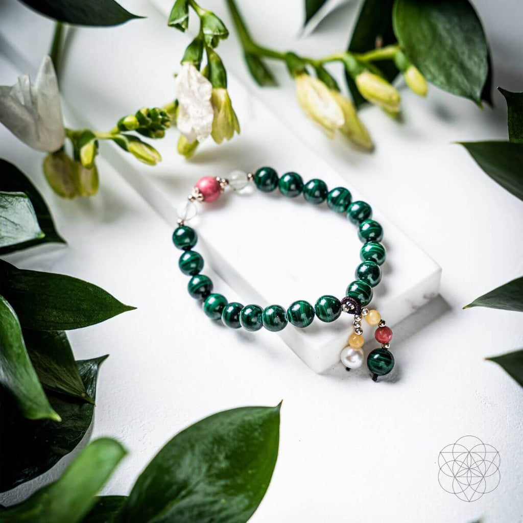 Green beaded bracelet with colorful charms on a white surface with green leaves.