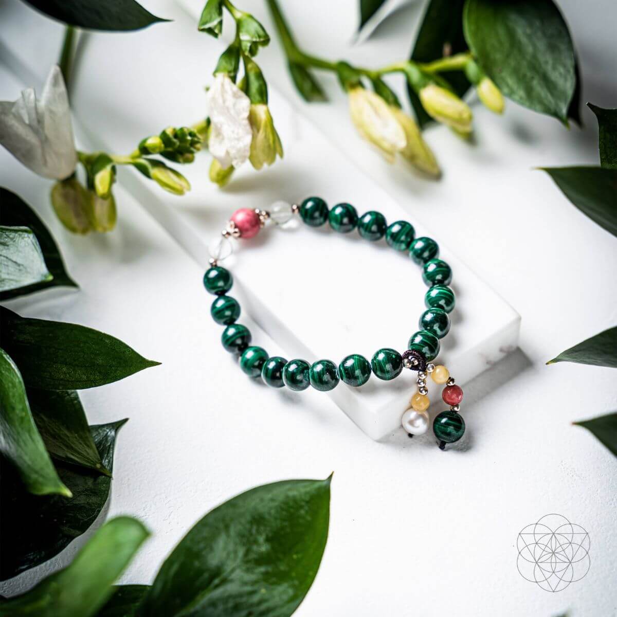 Green beaded bracelet with colorful charms on a white surface with green leaves.