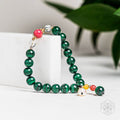 Green beaded bracelet with colorful accents on a white surface with a blurred green leaf background