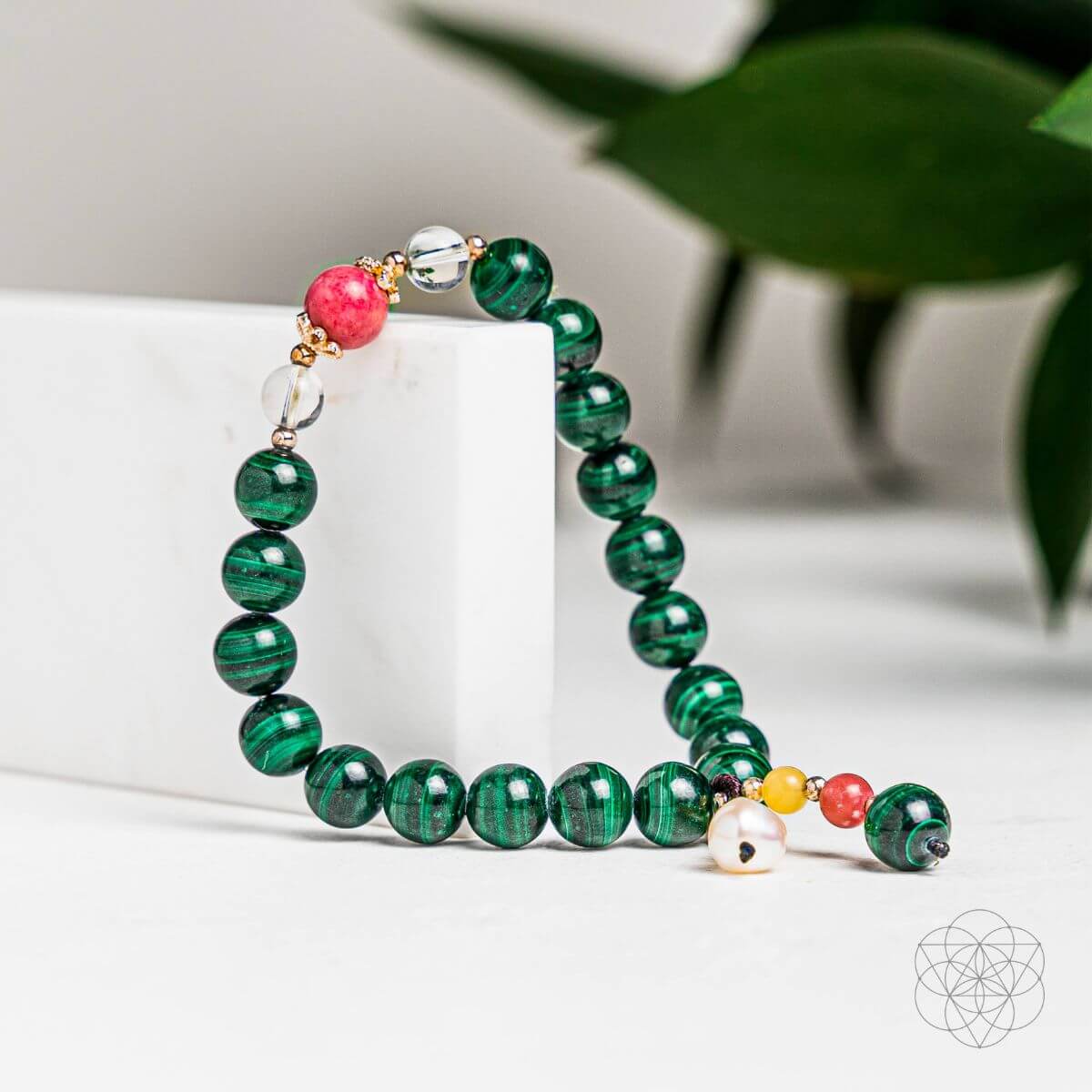 Green beaded bracelet with colorful accents on a white surface with a blurred green leaf background