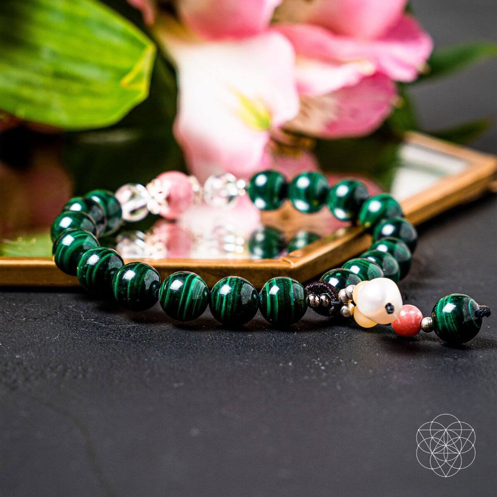 Green beaded bracelet with decorative beads on a dark surface with flowers in the background