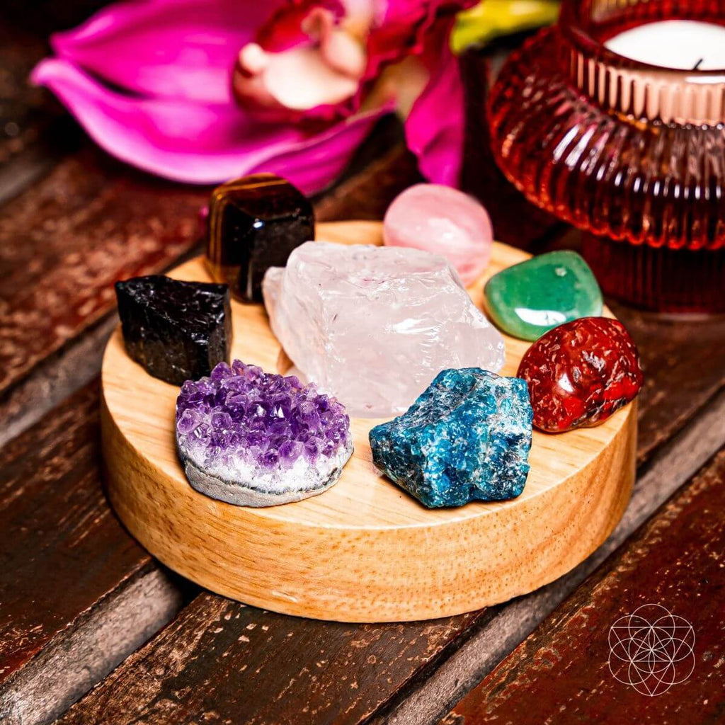Collection of colorful crystals on a wooden stand with a pink flower and candle in the background.