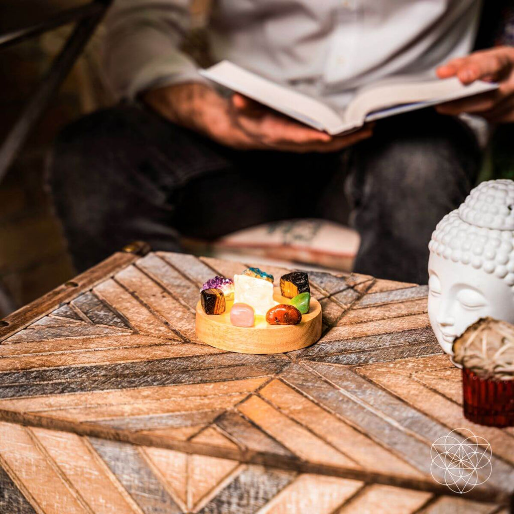 Person reading a book with a small decorative item and a Buddha statue on a wooden table.