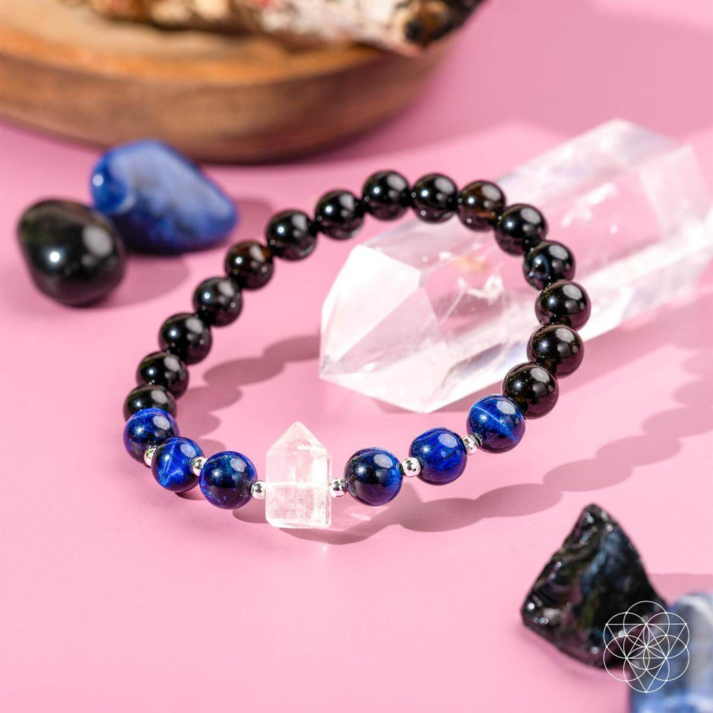 Glowing crystal bracelet with black, blue, and clear beads on a pink background