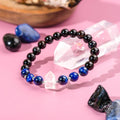 Glowing crystal bracelet with black, blue, and clear beads on a pink background