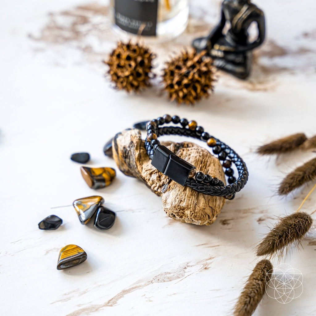 Black braided bracelet on a rock with tiger eye stones and natural elements on a light background
