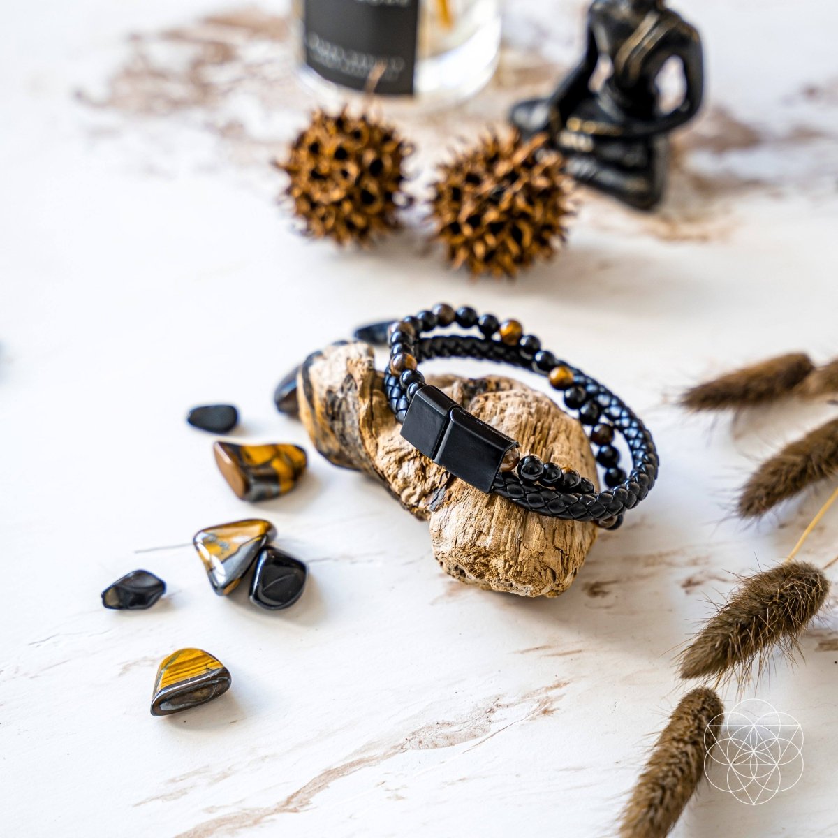 Black braided bracelet on a rock with tiger eye stones and natural elements on a light background
