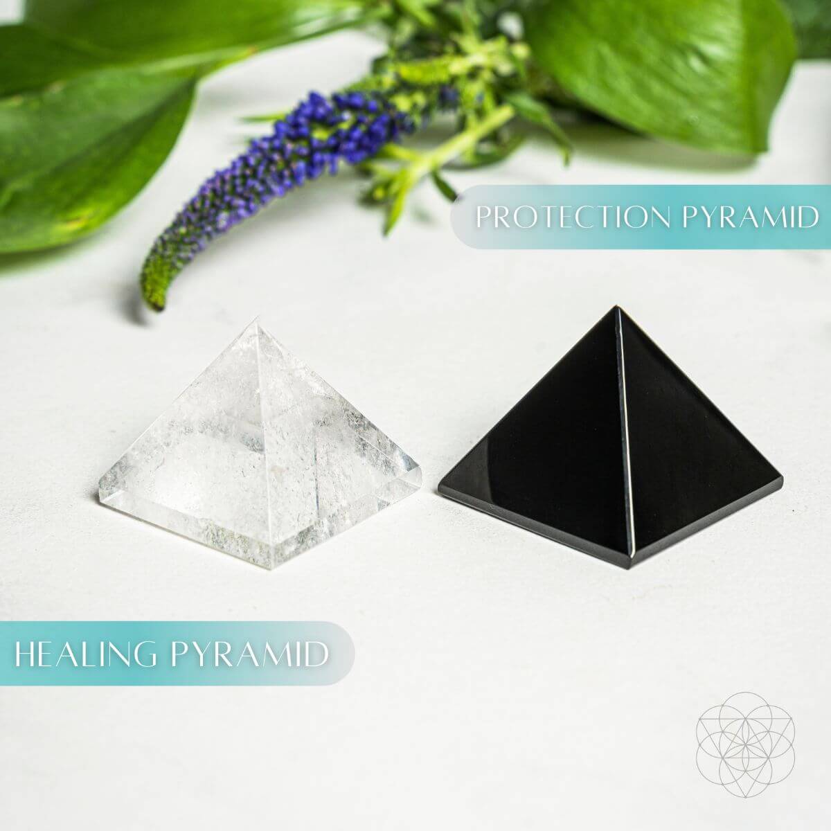 Two pyramid-shaped crystals labeled 'Healing Pyramid' and 'Protection Pyramid' on a white surface with green leaves and purple flowers.