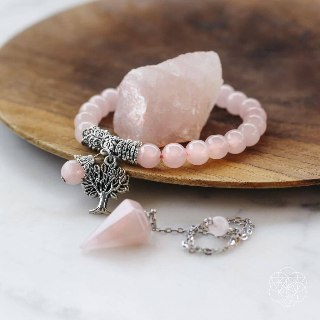 Pink beaded bracelet with tree of life charm on a wooden plate with rose quartz crystal