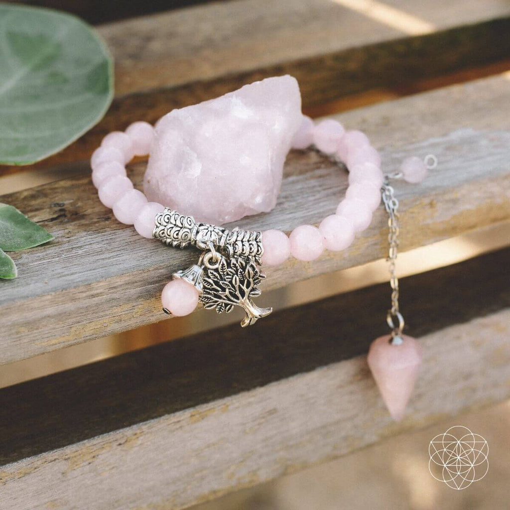 Pink beaded bracelet with tree charms on a wooden surface