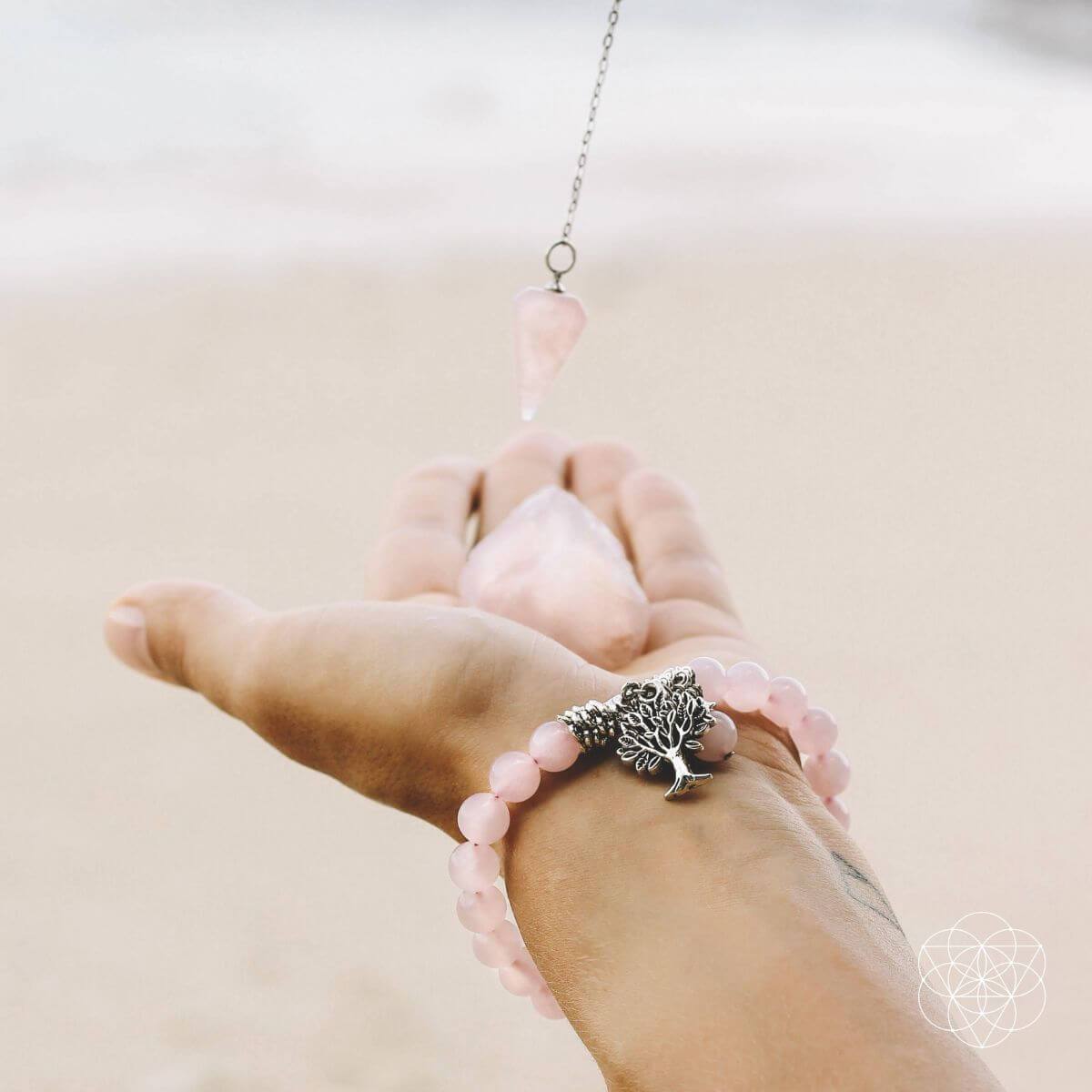 Hand wearing a pink beaded bracelet with a silver tree charm on a neutral background