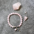 Pink beaded bracelet with tree of life charm and matching pendant on a gray surface