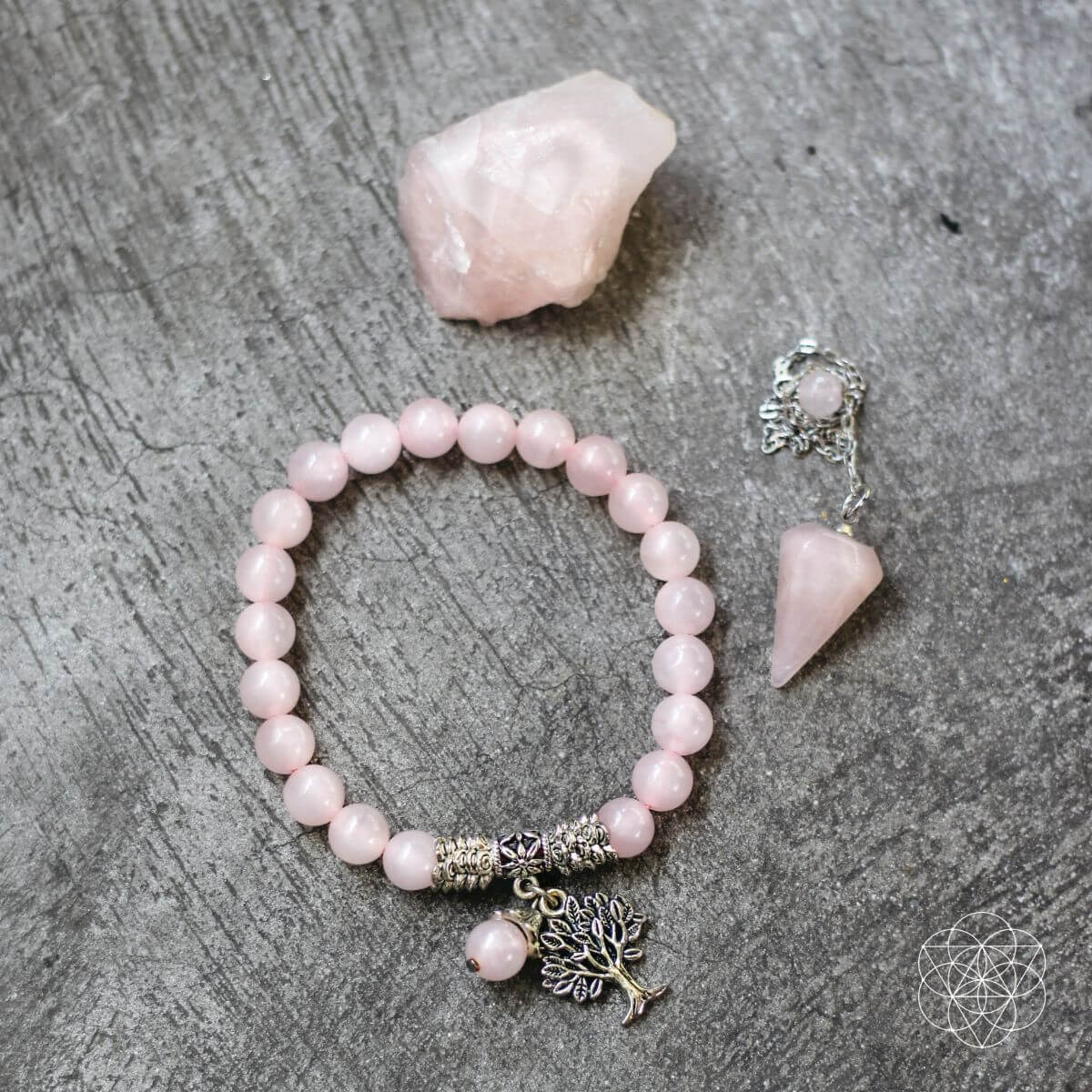 Pink beaded bracelet with tree of life charm and matching pendant on a gray surface