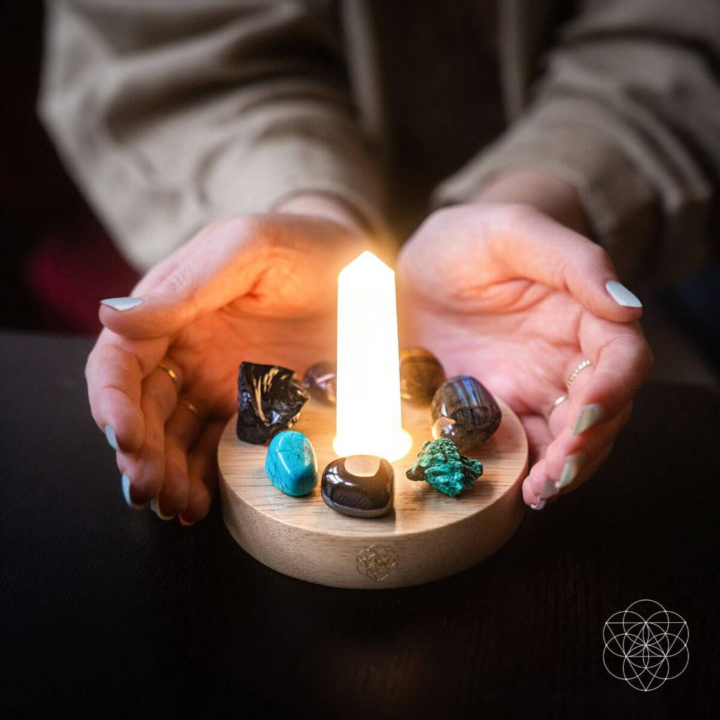 Hands holding a small wooden platform with a candle and crystals on a dark background