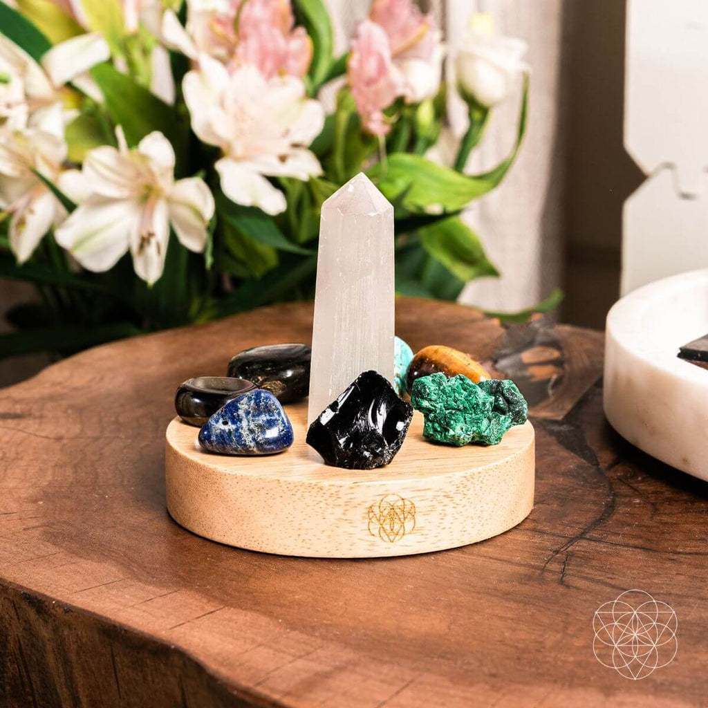 Crystal setup with a tall white crystal on a wooden stand, surrounded by various crystals and flowers in the background.