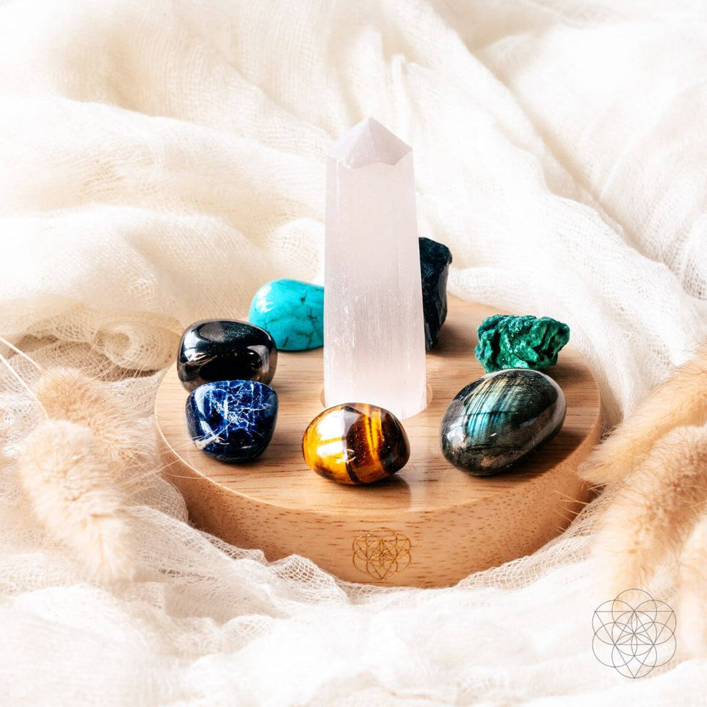 Set of colorful crystals on a wooden stand with a white candle, all on a soft fabric background.