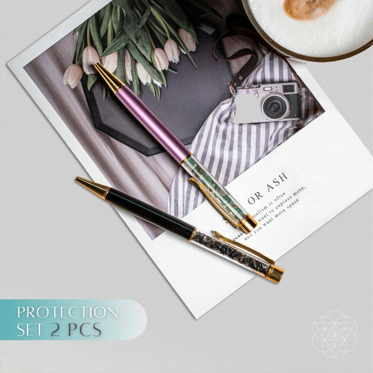 Two pens on a surface with a photo, camera, and coffee cup in the background.