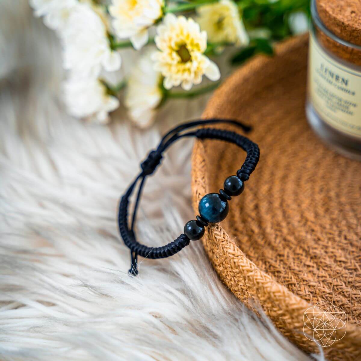 Black beaded bracelet on a fur surface with flowers and a jar in the background