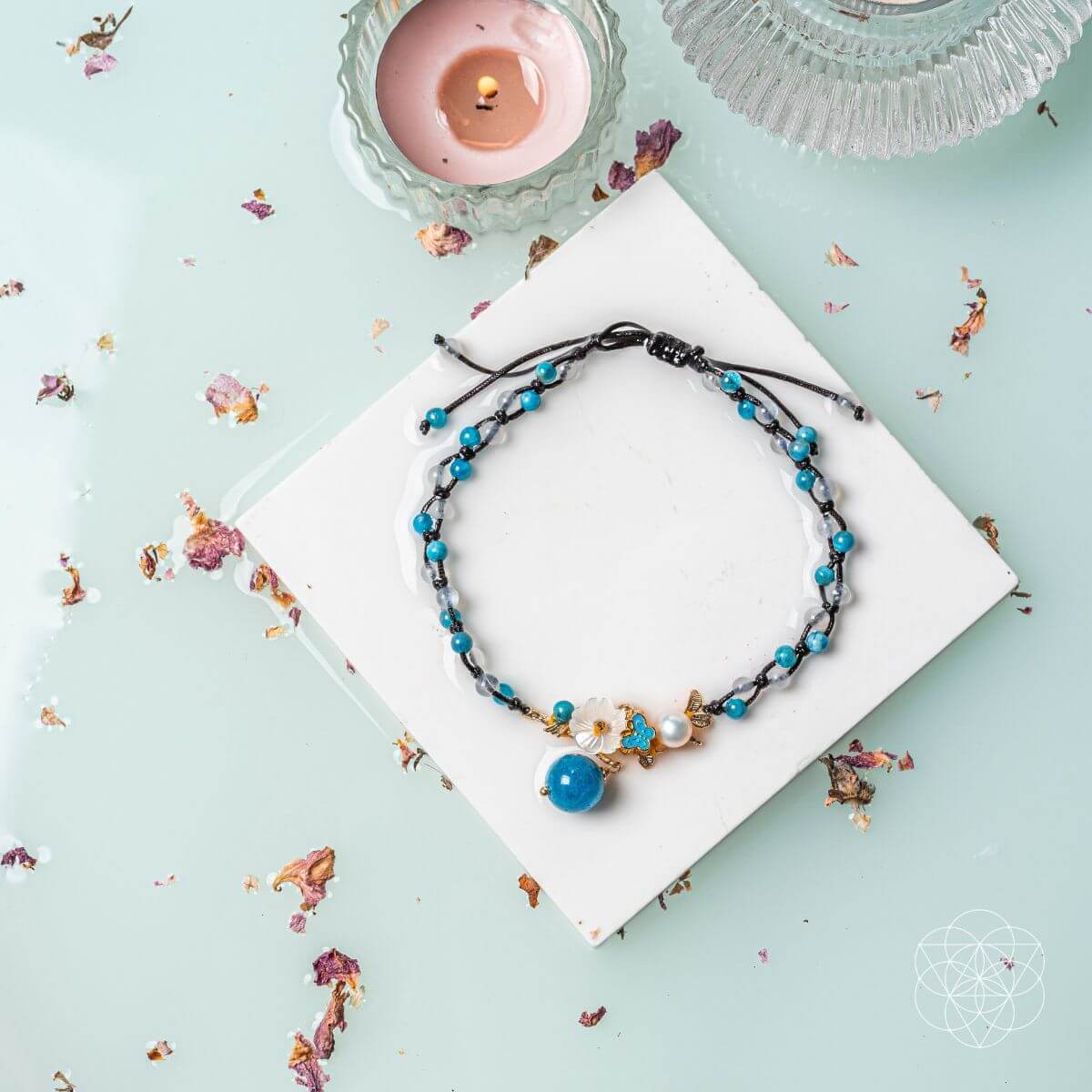 Necklace with blue and black beads on a white square with a candle and decorative elements on a light blue background