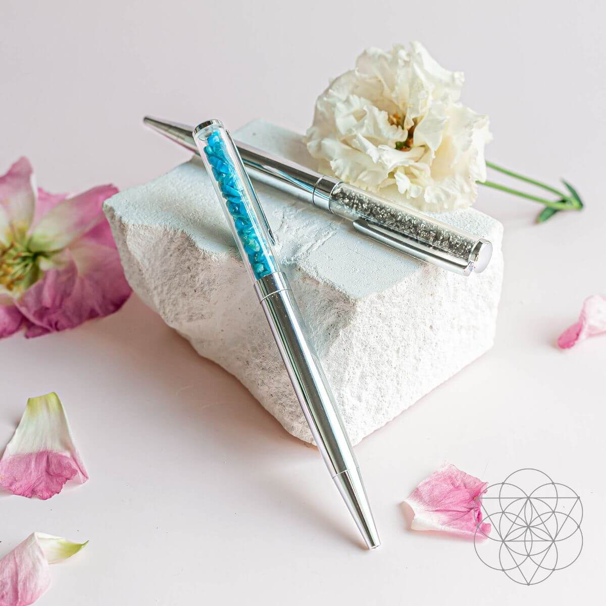 Silver pen with blue accents on a white stone block with flowers and petals.
