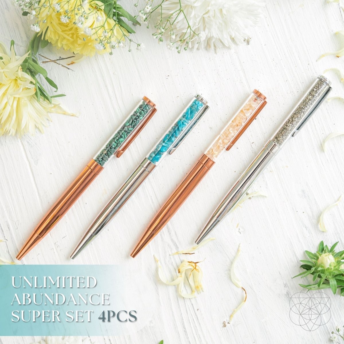 Set of four decorative pens with gemstone accents on a white surface with flowers.