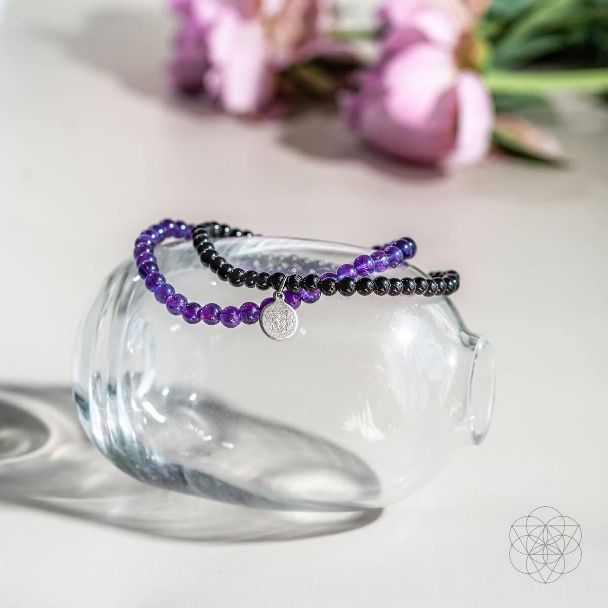 Purple beaded bracelet on a clear glass with pink tulips in the background