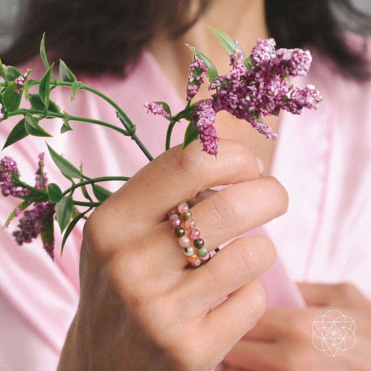 Hand holding a branch of purple flowers with a pink shirt in the background